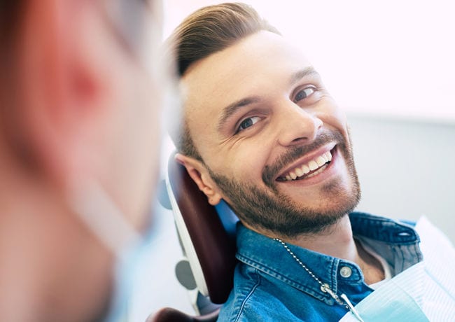 A male patient looks over at his dental care staff with a giant smile after having had bonding work performed on him.