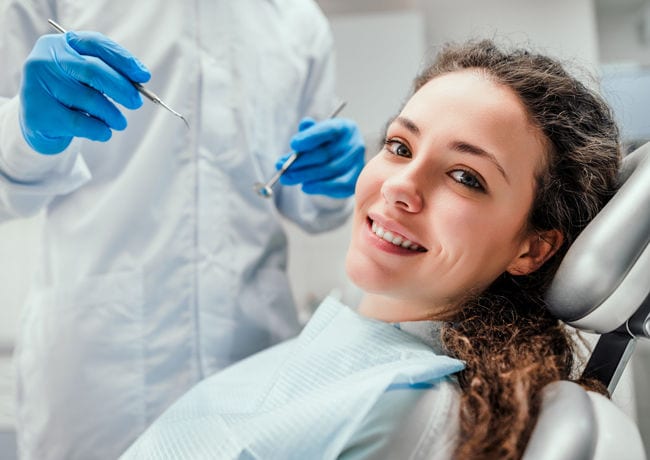 A female patient looks over to the camera wearing a paper apron as she prepares to get her teeth cleaned and examined.