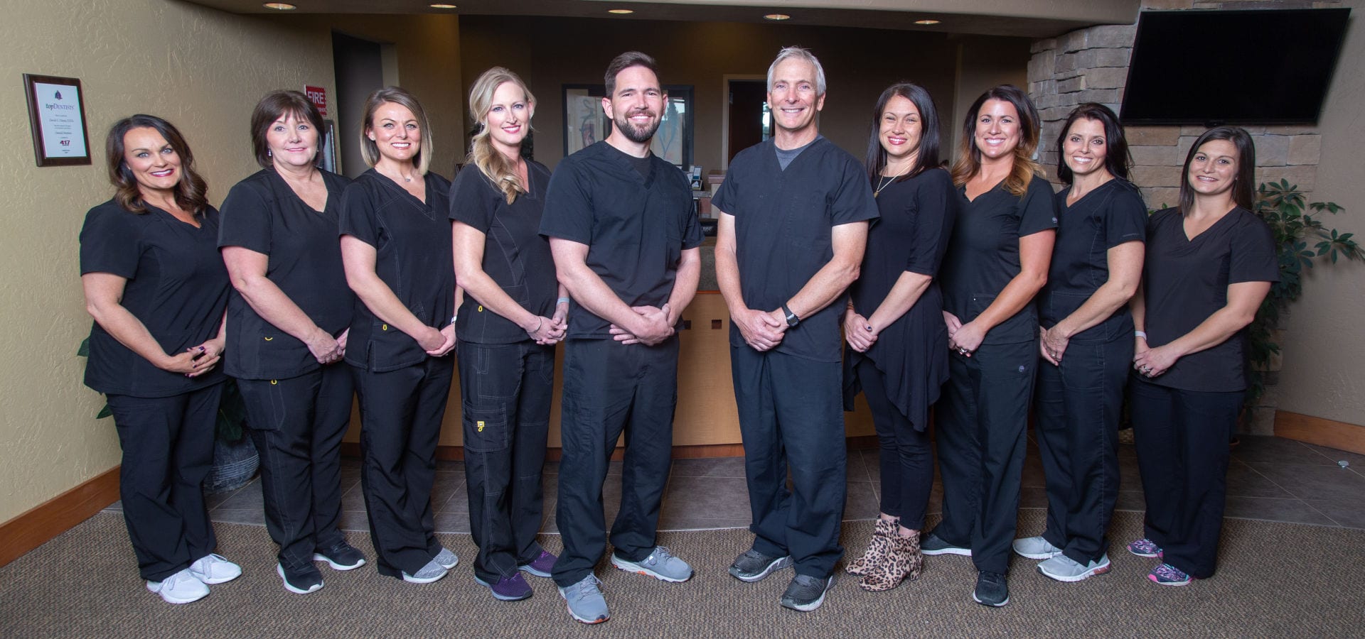 About 3 Dental office staff stand in front of the reception counter to pose for their photo, dentists at front center.