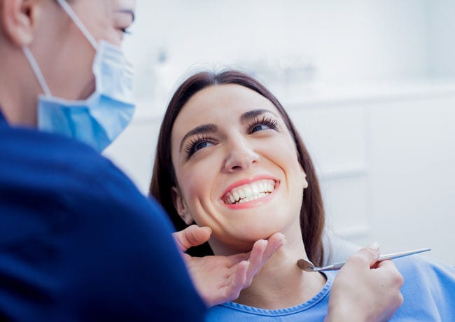 A female patient smiles excitedly as someone finishes performing teeth whitening work on her mouth.